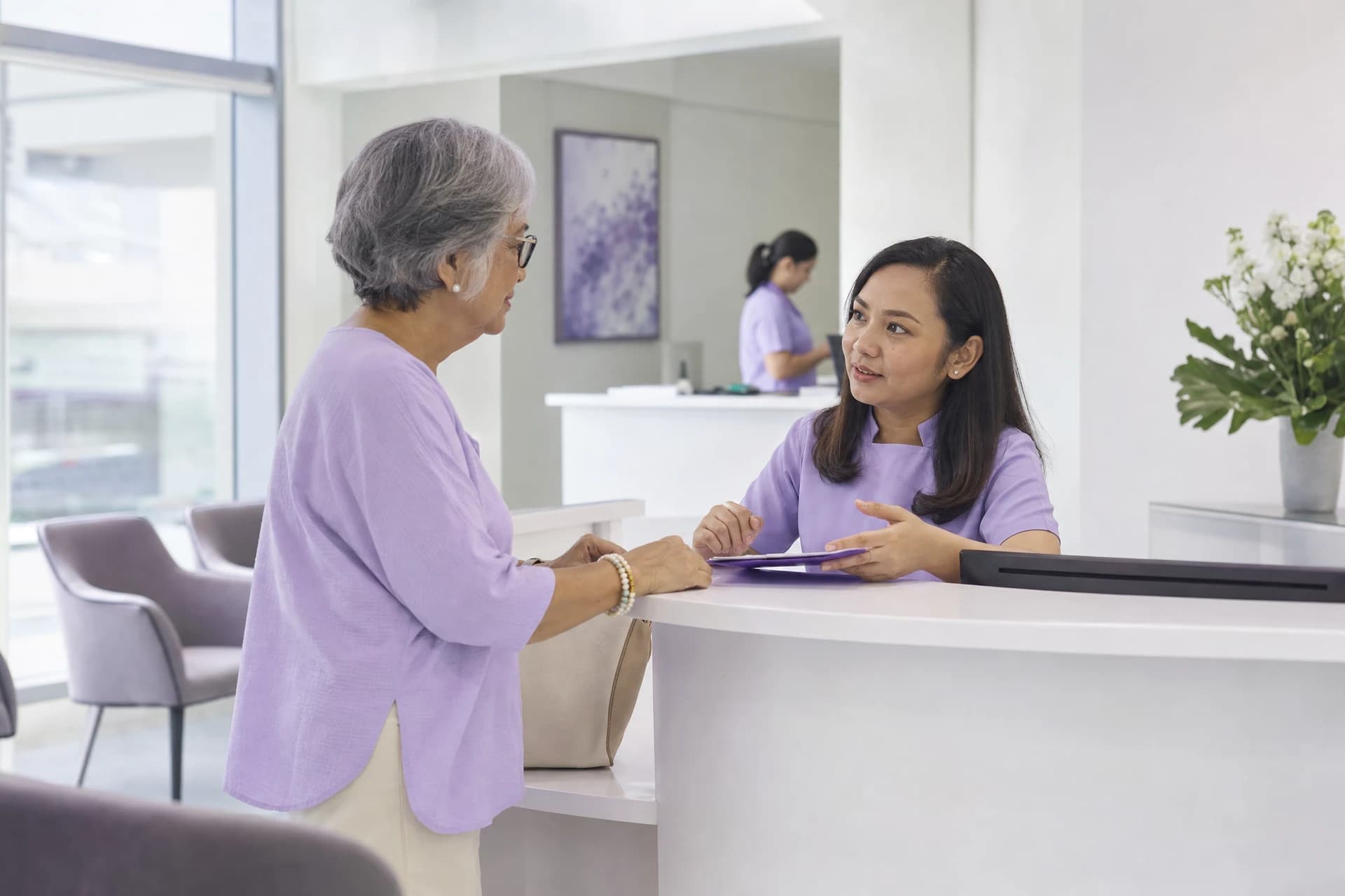 Clinic receptionist helping an older visitor with her appointment